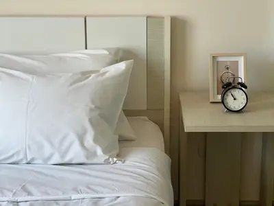 a bed with white sheets and a clock on a table at Cozy9Living in Bangkok 60mto MRT in Ban Bang Khwang