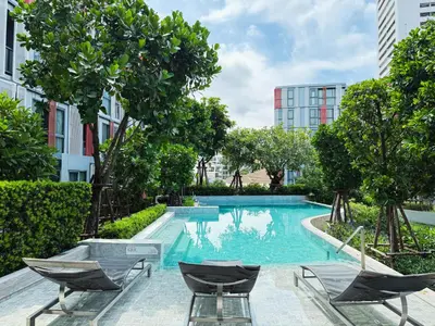 a swimming pool with chairs and trees and buildings at Near BTS l Workspace and Kitchen - Pool and Gym l Sontana in Bangkok