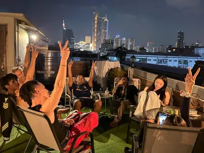 a group of people sitting on a roof with their hands in the air at Aura Hostel in Bangkok