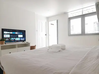 a white bedroom with a large bed and a flat screen tv at White House Ekkamai in Bangkok