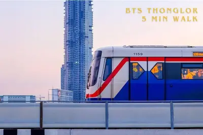 a train traveling on a bridge with a tall building at Contemporary Eastern 1BR 5 min BTS| All Essential in Khlong Toei