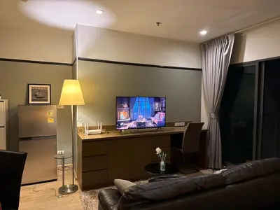 a living room with a couch and a desk with a television at Noble Remix Thong Lo Long Stay Cozy&Warm Direct access to BTS Pool Gym WiFi in Bangkok
