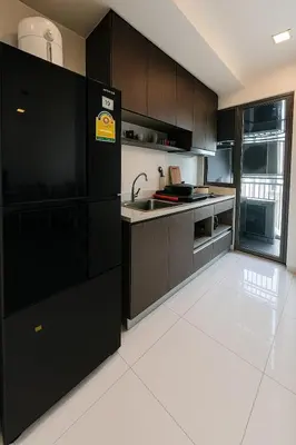 a kitchen with black cabinets and a white tile floor at The Monti Condo in Bangkok