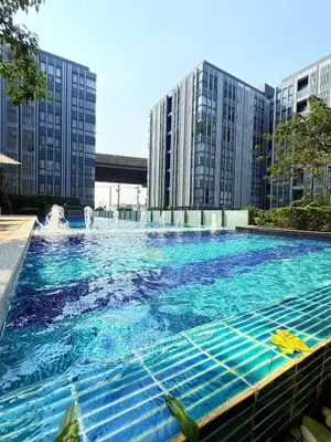 a large swimming pool with a fountain in front of buildings at The Monti Condo in Bangkok