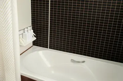 a white bath tub in a black tiled bathroom at The Wooden Nest Warm Stay at Sukhumvit 8 in Bangkok