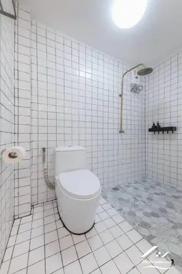 a white tiled bathroom with a toilet and a shower at Delightful Townhouse in the Heart of Sukhumvit in Bangkok