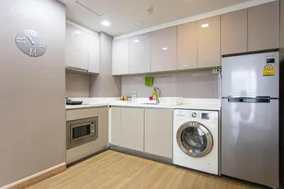 a kitchen with white cabinets and a washer and dryer at Dazzle Residence ByPinny in Bangkok