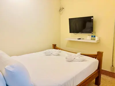 a bedroom with a bed with white sheets and a tv at Sukhum Charoen Krung Tak-Sin bridge guest house in Bangkok