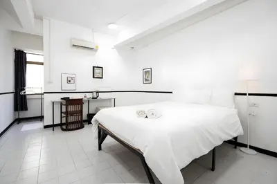 a white bedroom with a large bed and a table at XX GO INN MRT Hua Lamphong - วัดไตรมิตร in Samphanthawong