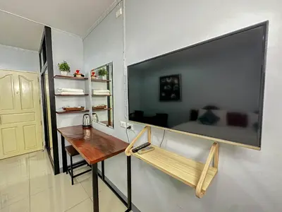 a room with a table and a large television on the wall at Nuanchan Apartment in Ban O Pao