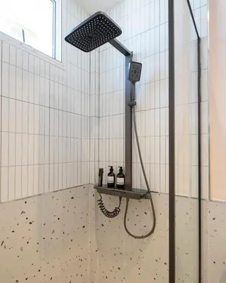 a shower in a bathroom with white tiled walls at Bembis Hotel Charoenakorn 10 in Chinatown