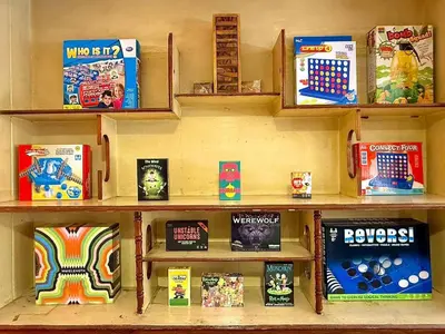 a shelf filled with games and books on a wall at Super BIG Mid Century Home near River & IconSiam in Khlong San