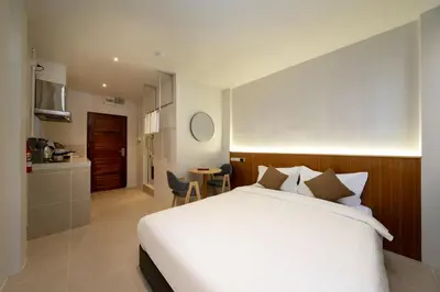 a bedroom with a large white bed and a kitchen at OH Suites 72 in Bangkok
