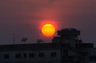 a sun setting over a building with a red sky at Thanabhumi in Bangkok