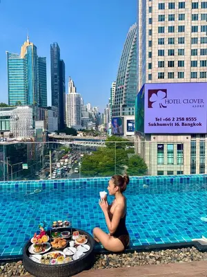 a woman sitting next to a pool with a tray of food at Hotel Clover Asoke - SHA Extra Plus in Bangkok