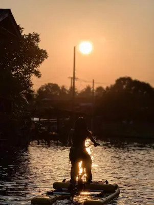 a person riding a paddle board in the water at sunset at นำสมัย สุขใจ สนามชัย in Bangkok