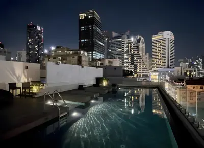 a rooftop pool with a city skyline at night at Designer Home BTS bangkok centre Pool Gym