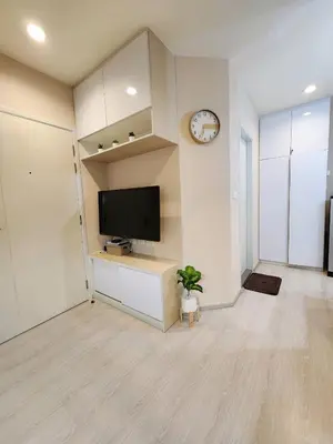 a living room with a television and a clock on a wall at Homely Condo Minimal Style Near BTS Silom line in Bang Khun Thian