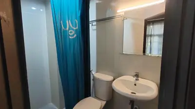a bathroom with a toilet and a sink with a blue shower curtain at Bed's Friend in Bangkok