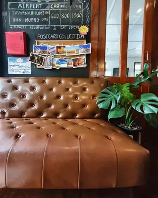 a brown leather couch sitting in a room with a plant at Dinsomon Hotel in Bangkok