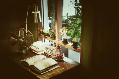 a table with books and a window with plants at Yoo Yen Pen Sook in Bangkok