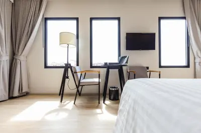 a bedroom with a bed and a desk and windows at Mii Hotel Srinakarin in Bangna