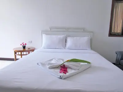 a white bed with a white robe with a pink flower on it at JL Bangkok Hotel in Bangkok
