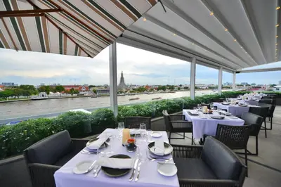a restaurant with tables and chairs with a view of a river at Riva Arun Bangkok in Bangkok