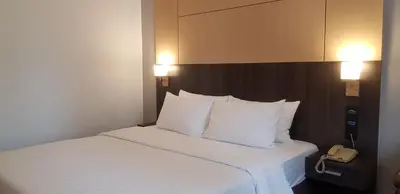a bedroom with a bed with white sheets and a phone at Ariston Hotel Bangkok in Bangkok