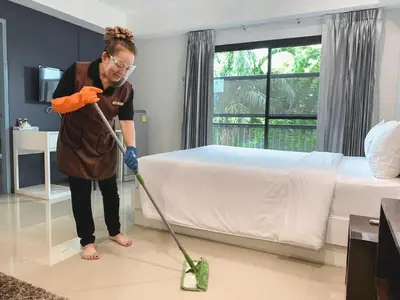 a woman vacuum cleaning a bedroom with a mop at Casa Residence Hotel in Bangkok