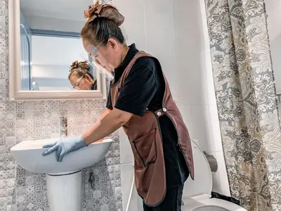 a woman is washing a sink in a bathroom at Casa Residence Hotel in Bangkok