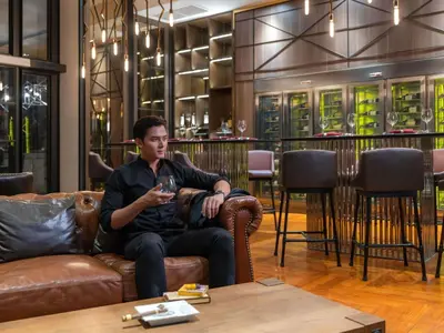 a man sitting on a couch with a glass of wine at Mercure Bangkok Makkasan in Bangkok