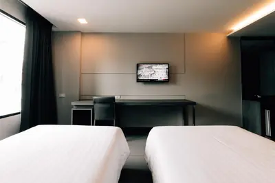 a room with two beds and a desk and a television at Spenza Hotel in Bangkok
