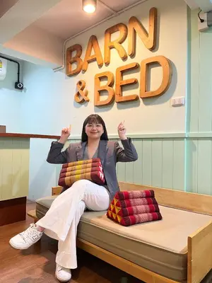 a woman sitting on a bed in a bar and beer sign at Barn & Bed Hostel in Bangkok