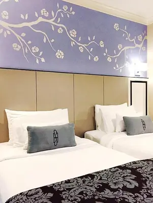 two beds in a hotel room with a painting on the wall at Sara's Hotel in Bangkok