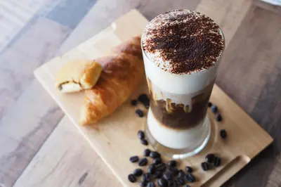 a drink on a wooden cutting board with a croissant and a dessert at GN Luxury Hostel in Bangkok