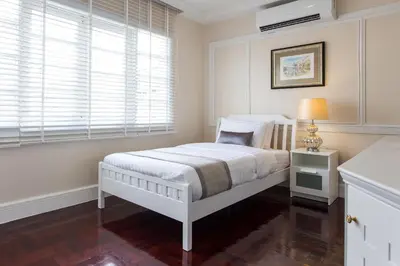 a white bedroom with a bed and a window at The Lek Aree in Bangkok