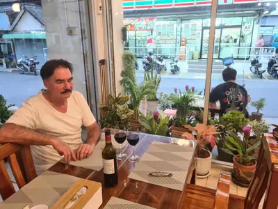 a man sitting at a table with a bottle of wine at Roong-Arun Apartment in Bangkok