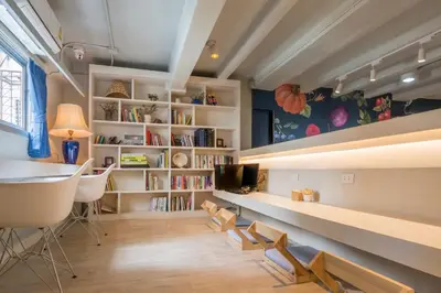 a room with a library with white chairs and bookshelves at Kinnon Deluxe Hostel Coworking Cafe in Bangkok