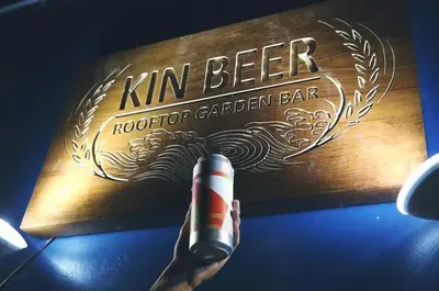 a hand holding a bottle of kunin beer on a table at Kinnon Deluxe Hostel Coworking Cafe in Bangkok