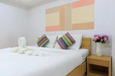 a white bed with pillows and a vase of flowers at Jr Mansion On Nut Soi 25 in Bangkok