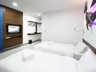 a white bedroom with two beds and a tv at Anna-Nava Pakkret Hotel in Nonthaburi