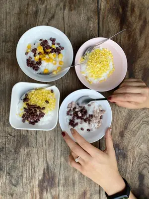 a woman holding four plates of food on a table at Issara by D Hostel in Bangkok