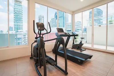 a gym with cardio equipment in a room with windows at The Bless Hotel and Residence in Bangkok