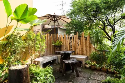 a garden with two benches and an umbrella in front of a fence at Nappark Hostel @Khao San in Bangkok
