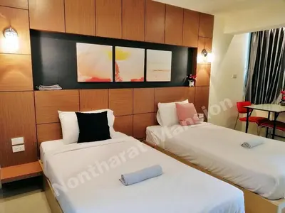 two beds in a room with a tv on the wall at Nontharat Mansion in Nonthaburi