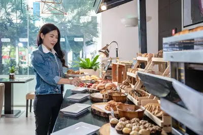 a woman standing in a bakery preparing food at Marriott Executive Apartments Sukhumvit Park, Bangkok in Bangkok