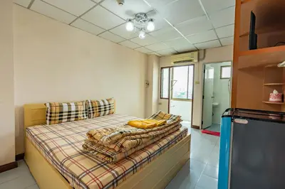 a bedroom with a bed with blankets and a refrigerator at Tat Hotel in Bangkok