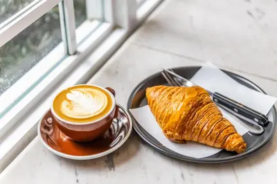 a plate with a cup of coffee and a croissant at Baan 2459 Heritage House in Bangkok