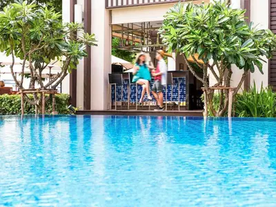 two girls sitting on chairs next to a swimming pool at Ibis Bangkok Riverside in Bangkok